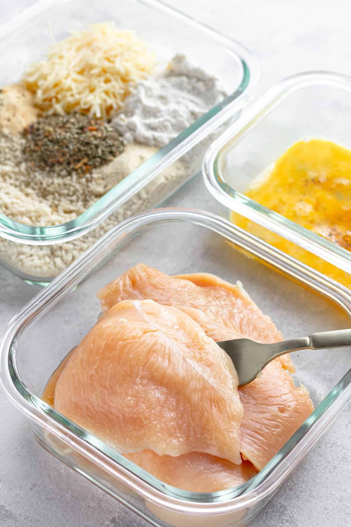 Three Glass Containers on a Counter – One Containing Raw Chicken, One Containing the Egg Mixture and One Containing the Un-Combined Breading Mixture