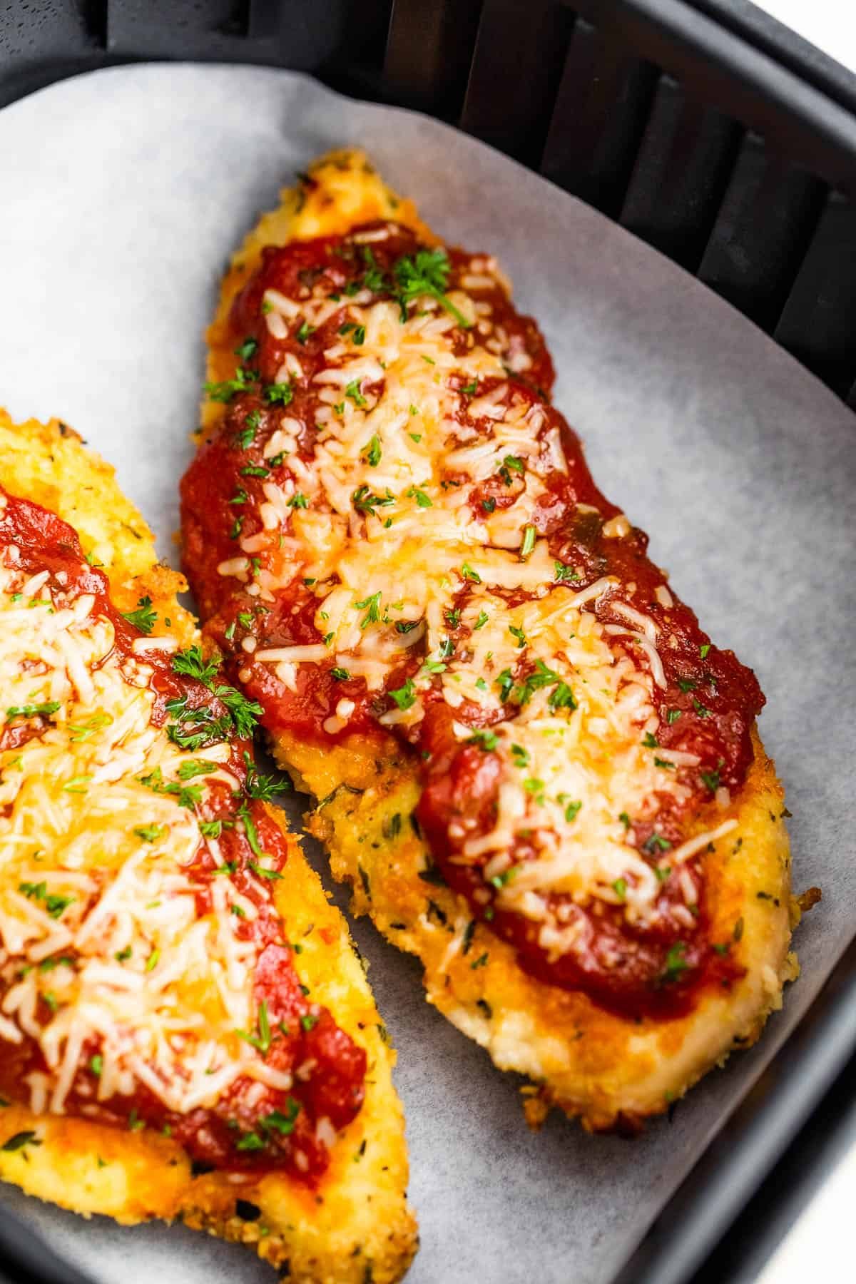Two Pieces of Breaded, Partially Cooked Chicken Being Topped with Marinara and Shredded Parmesan Cheese