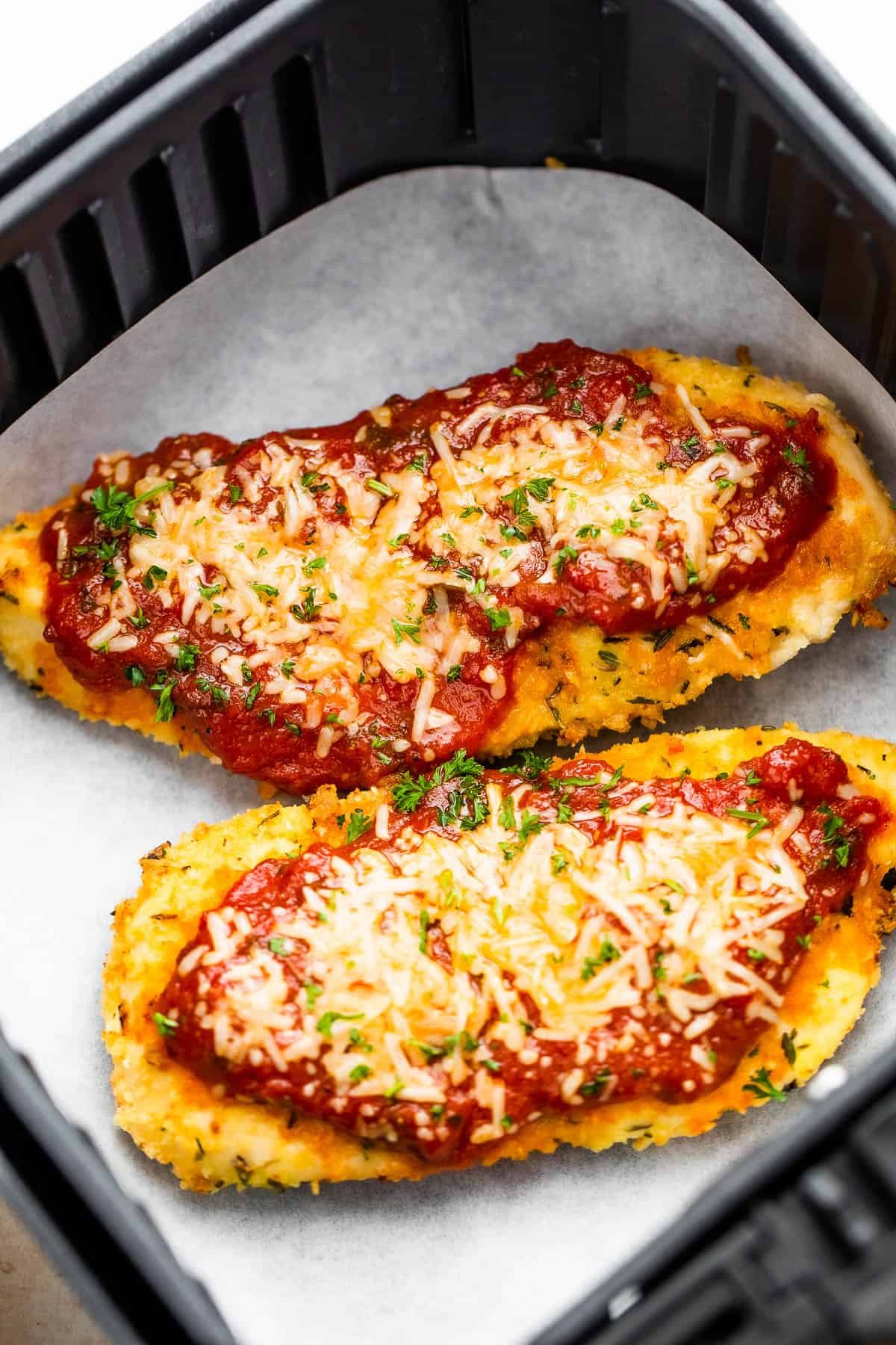 Two Pieces of Breaded, Partially Cooked Chicken Being Topped with Marinara and Shredded Parmesan Cheese