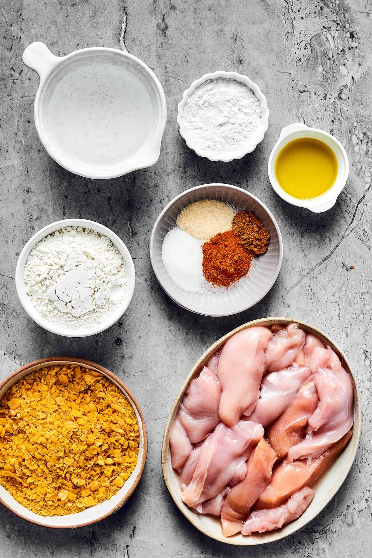 From top: Water, tapioca flour, olive oil, all-purpose flour, seasonings, corn flakes, chicken breast strips.