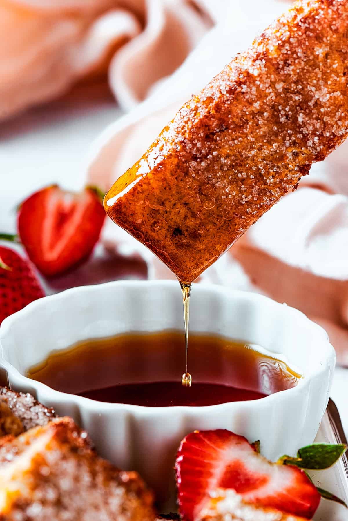 Lifting a piece of toast from a cup of syrup, with the syrup dripping back into the cup.