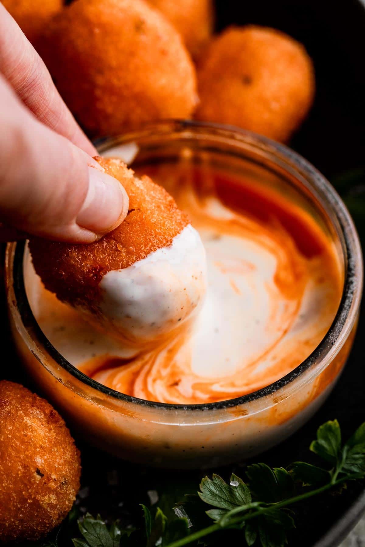 A Hand Dipping a Jalapeno Popper into a buffalo ranch sauce.