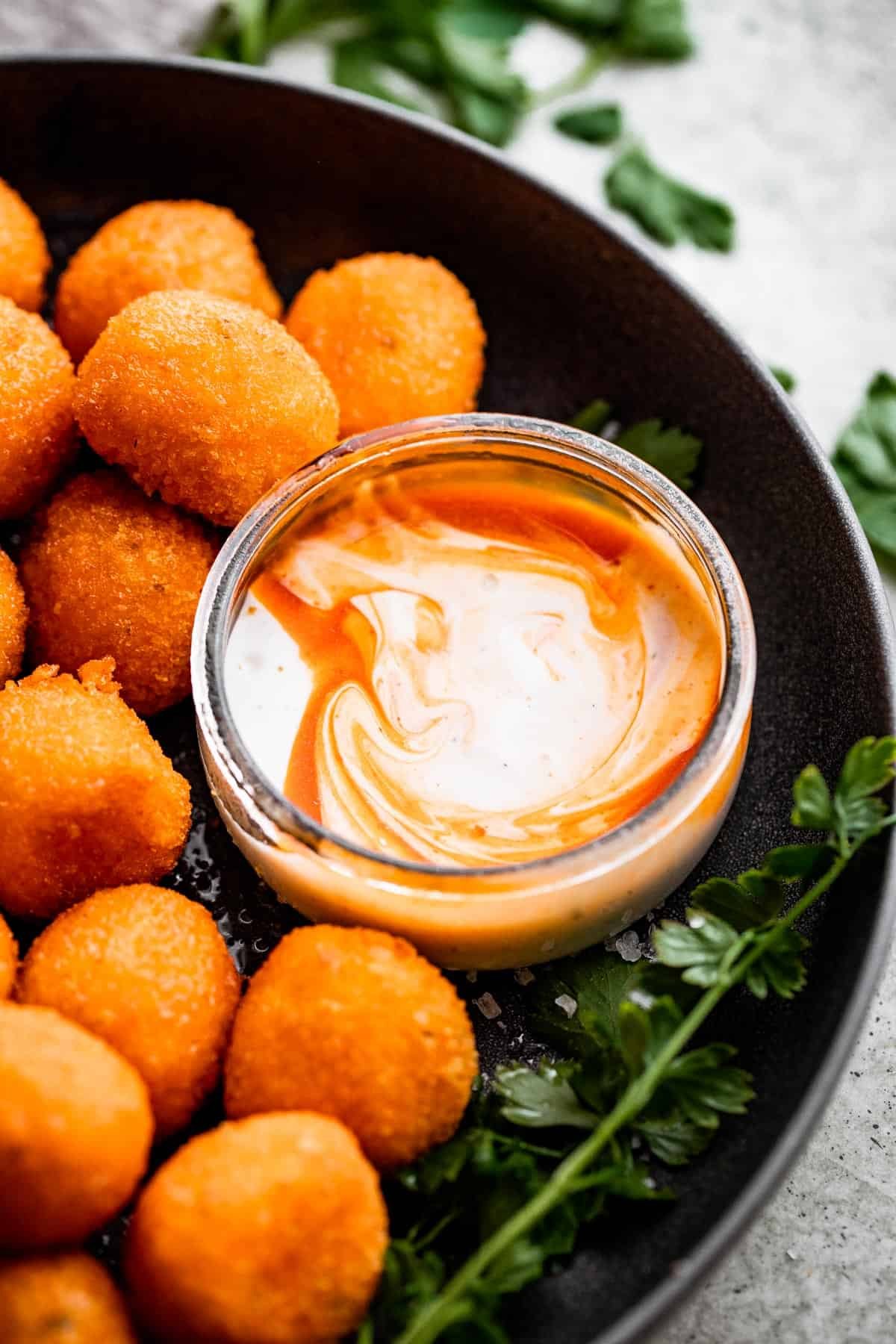 a black serving bowl with air fried jalapeno popper balls and a smaller glass bowl with dipping sauce.