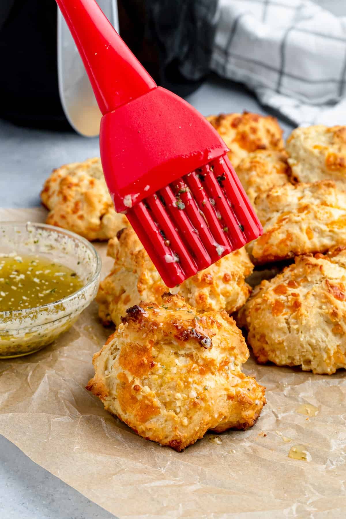 Garlic Butter Being Brushed Over an Air Fryer Biscuit with a Red Pastry Brush
