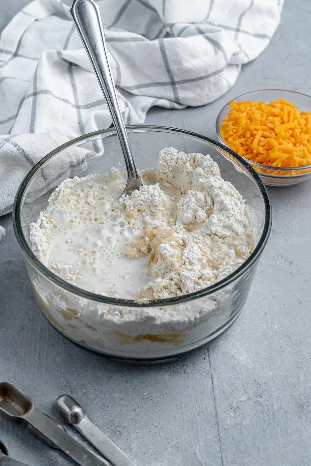 Bisquick Mix, Milk and Butter in a Bowl Beside a Dish of Shredded Cheddar