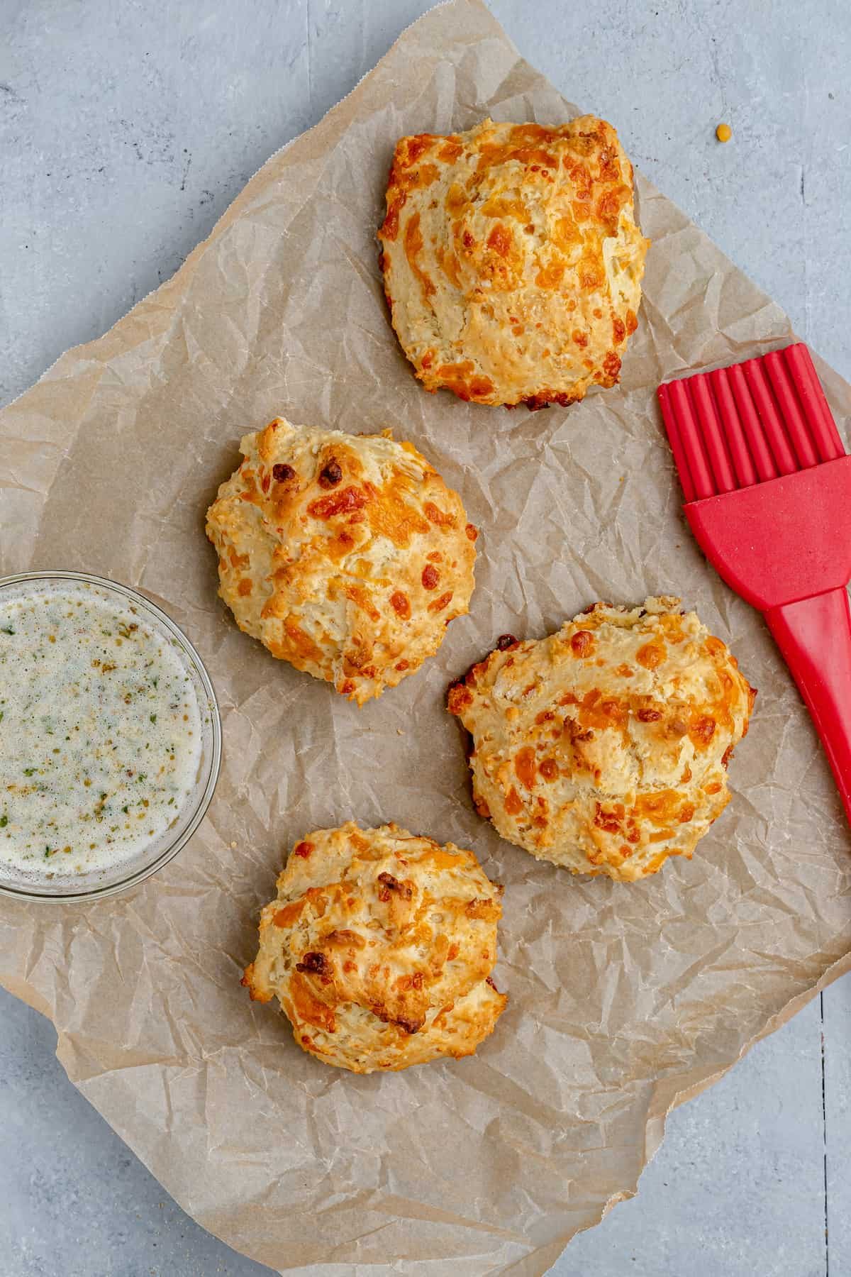 Four Air Fryer Biscuits on a Sheet of Parchment Paper with a Pastry Brush and a Small Dish of Garlic Butter