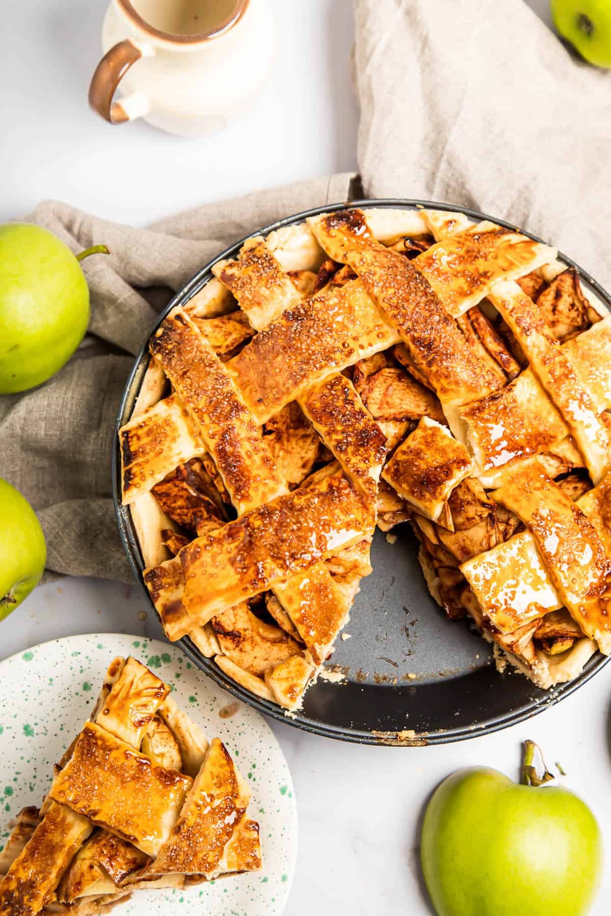 An apple pie with a slice cut out of it. The slice is on a saucer nearby.