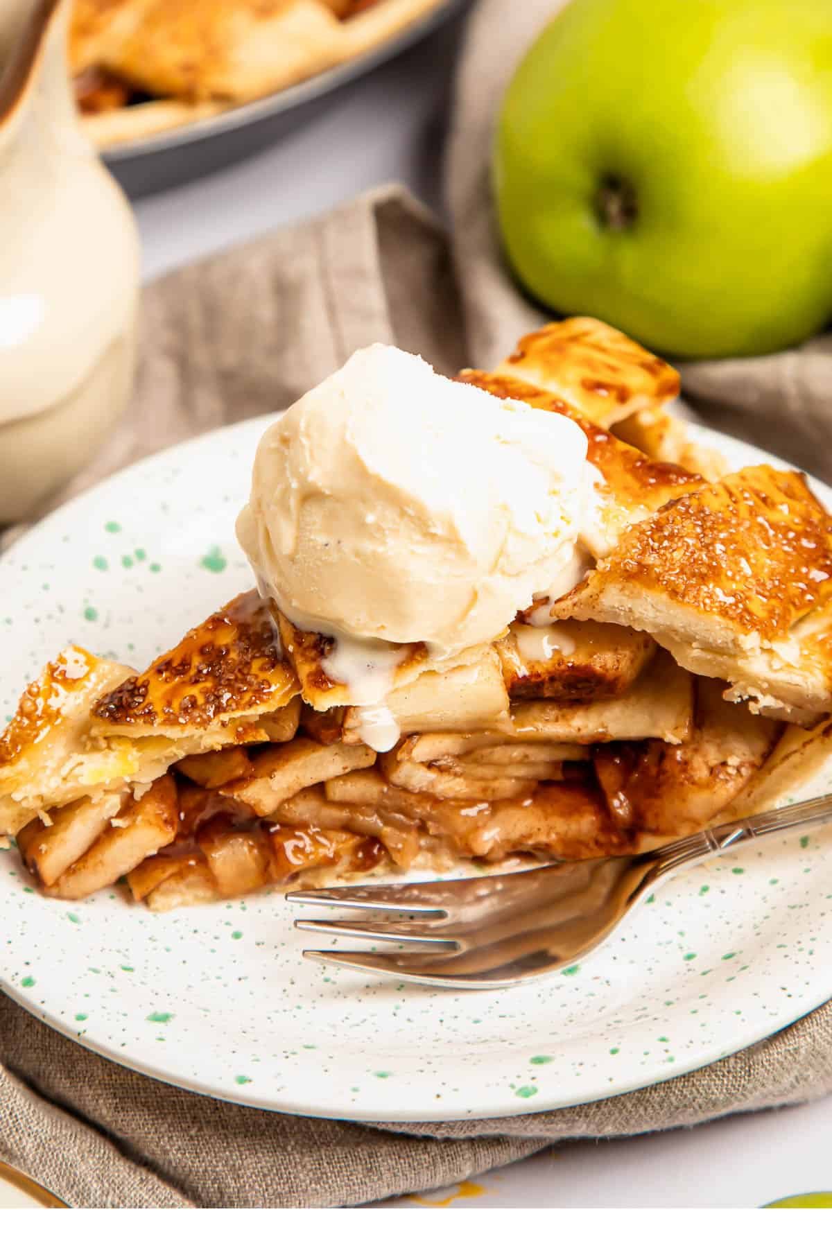 a slice of apple pie topped with ice cream on a plate with a fork
