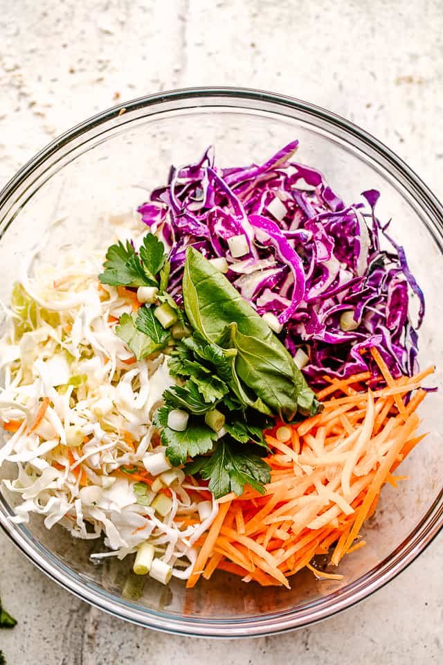 shredded red and green cabbage in a glass bowl with shredded carrots and fresh cilantro.