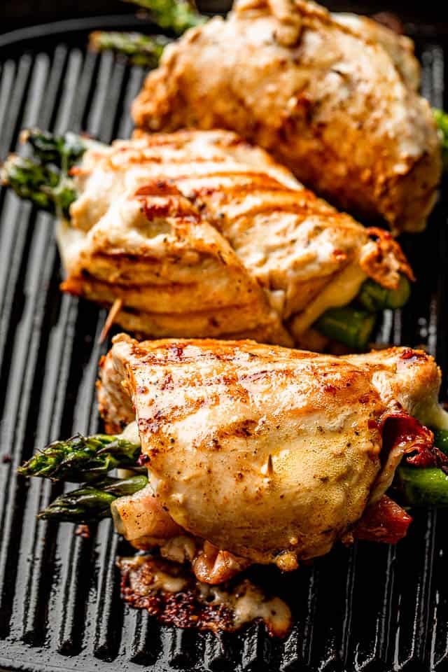 three chicken roll ups stuffed with asparagus, prosciutto, and cheese, and cooking on a grill pan