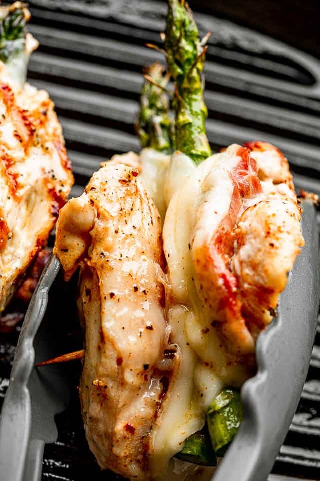 chicken breast stuffed with prosciutto, cheese, and asparagus held together with a pair of tongs