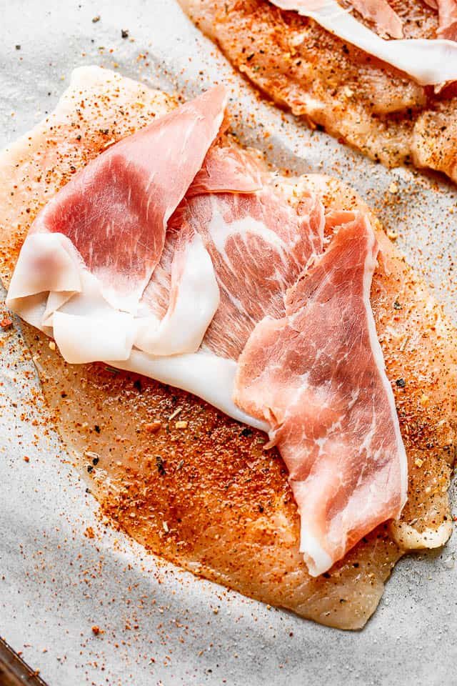 slice of prosciutto set over a raw chicken breast