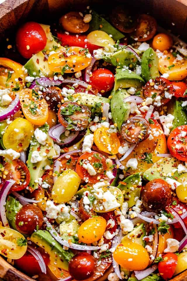 top shot of a wooden salad bowl filled with tomatoes, onions, avocado, and bleu cheese