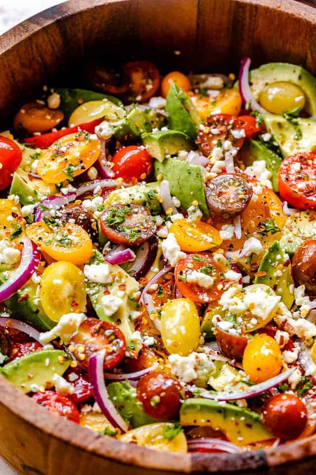 side shot of wooden salad bowl filled with tomatoes, onions, avocado, and bleu cheese