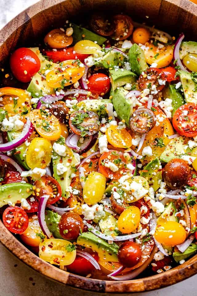 diced avocados, sliced tomatoes, sliced onions, and crumbled cheese in a wooden salad bowl