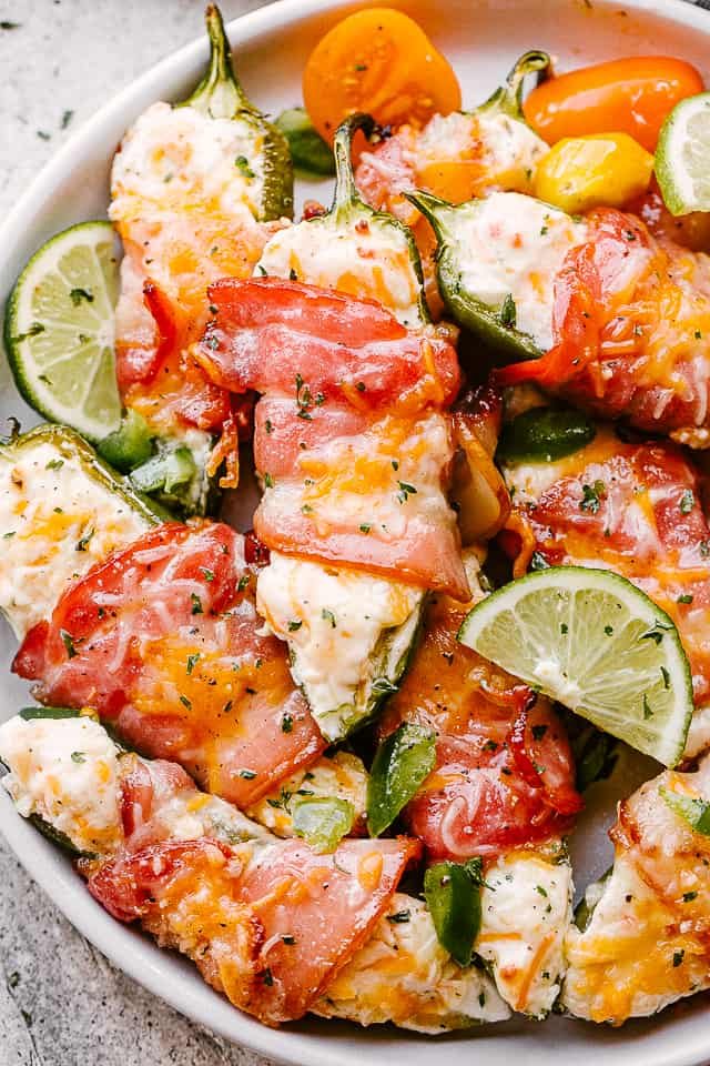 Baked jalapeno poppers on a white serving dish, garnished with herbs and lime wedges.