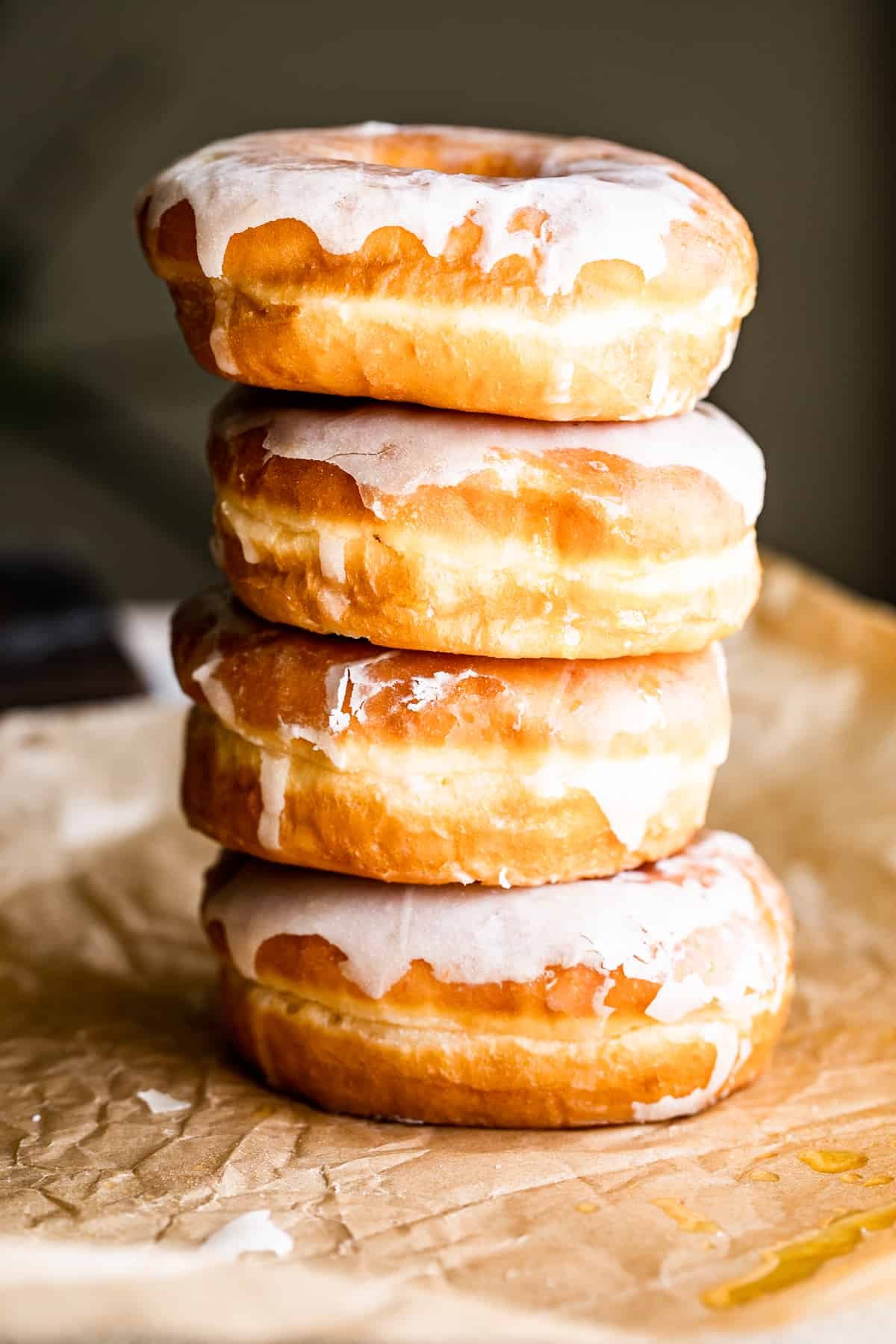 four apple cider doughnuts stacked one on top of the other, and pictured against a brown backdrop.
