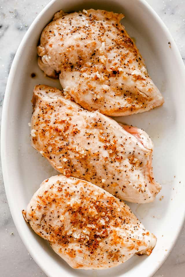 top view of seasoned chicken breasts in a white oval baking dish