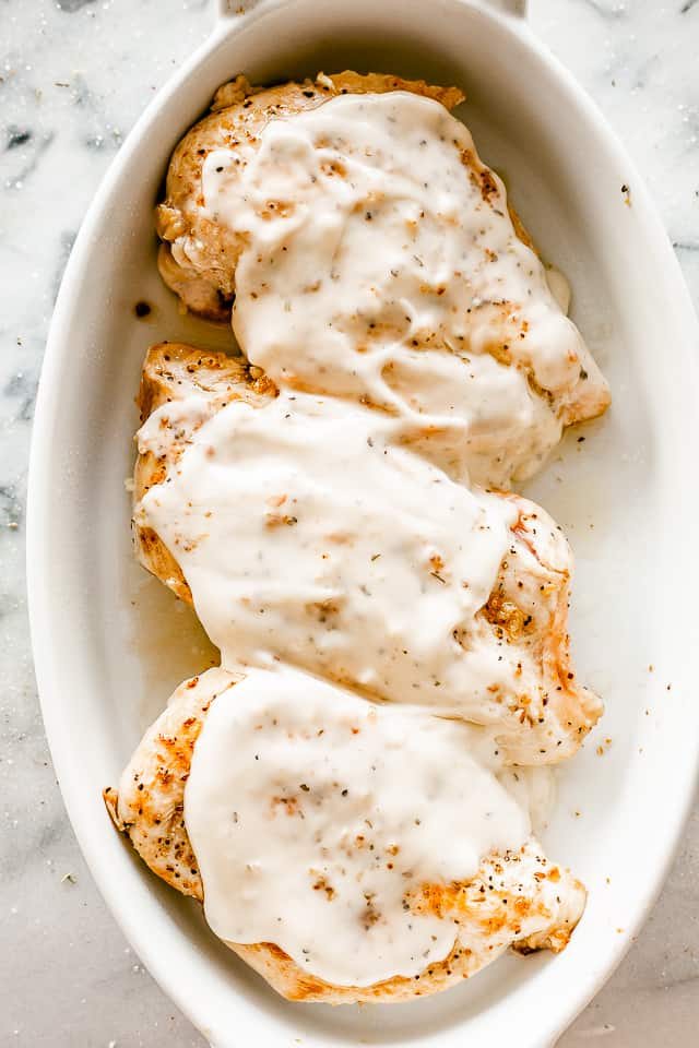 browned chicken breasts in a white baking dish topped with caesar dressing
