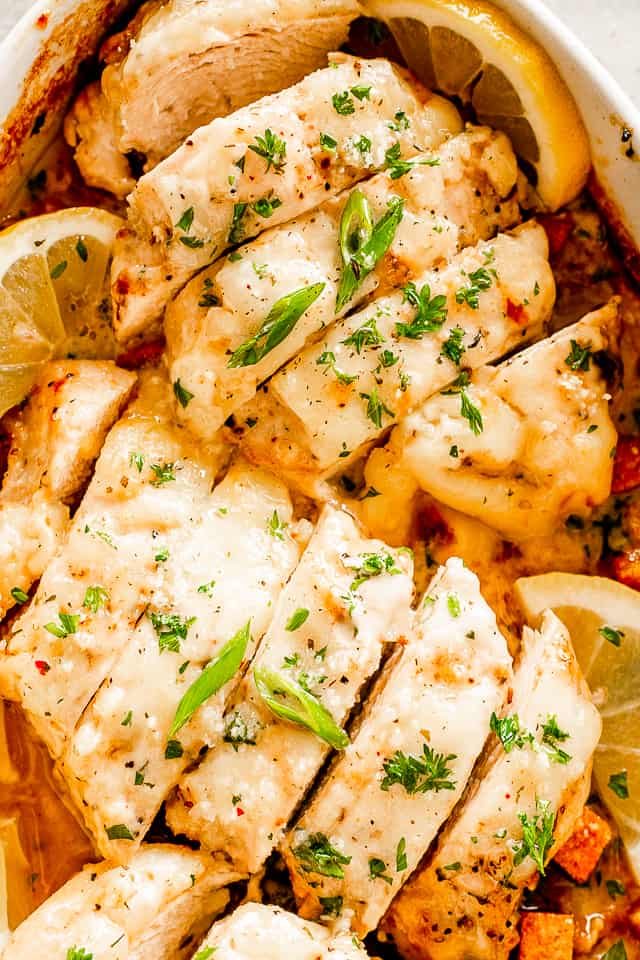 close up shot of sliced baked chicken breasts topped with caesar dressing and parsley