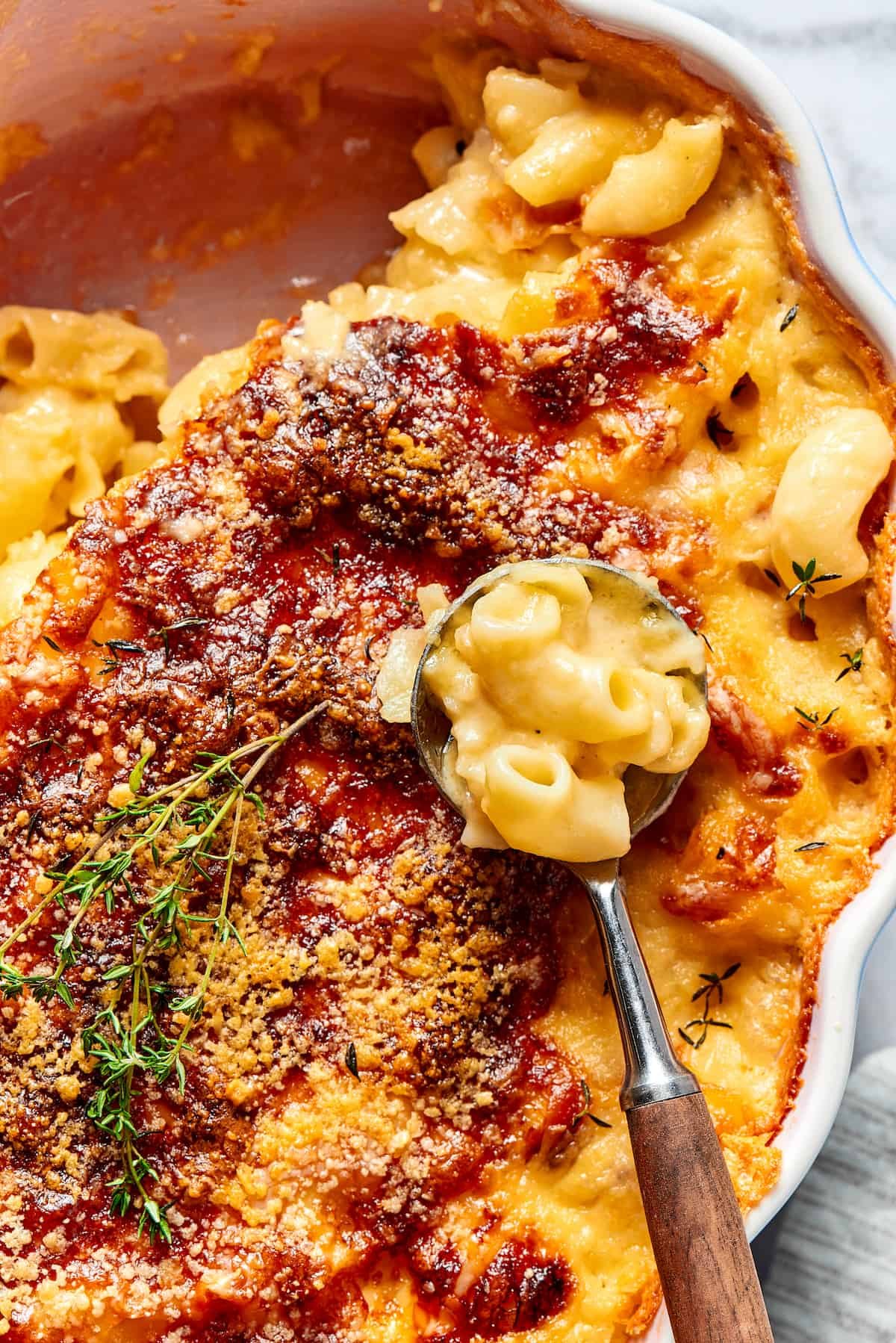 A baking dish of mac and cheese with some of it spooned out of the corner. A serving spoon with is resting in the dish.