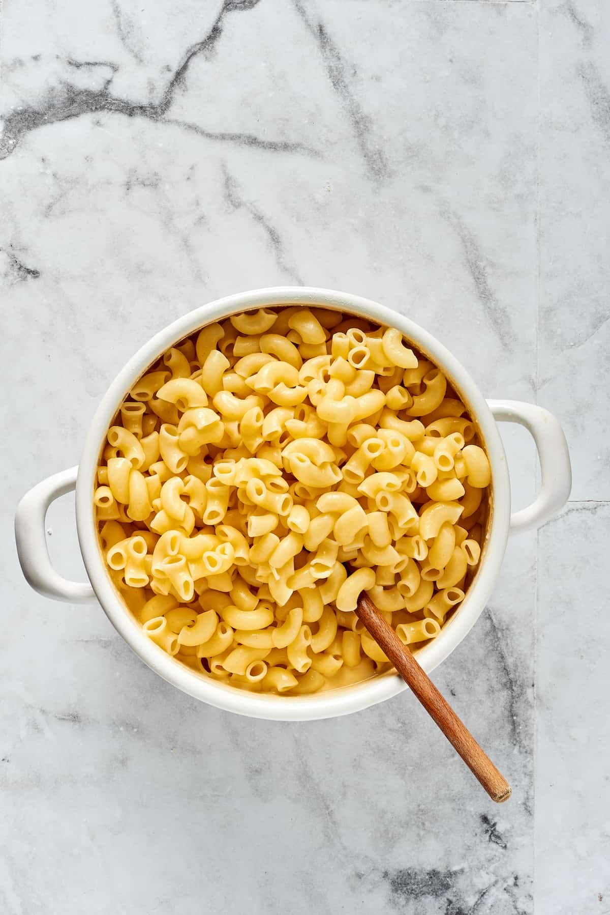 Stirring cooked elbow pasta into cheese sauce.