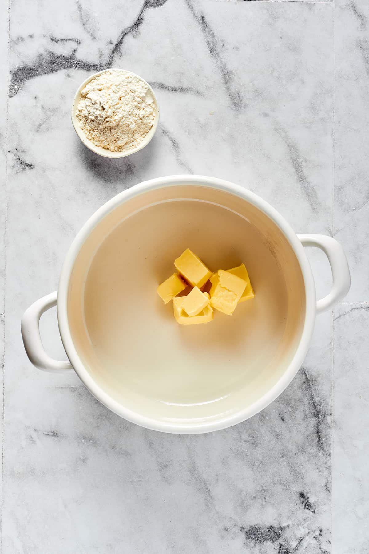 Butter melting in a Dutch oven, next to a small dish of flour.
