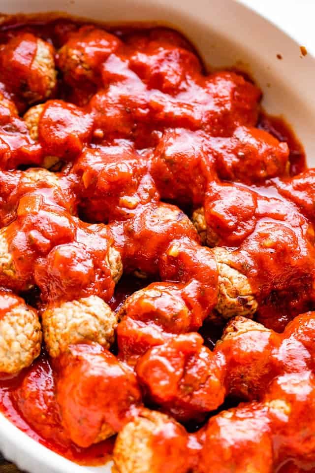 pouring marinara sauce over meatballs