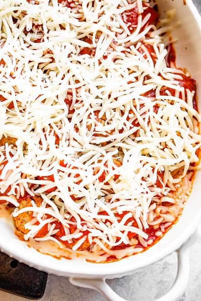 prepping to bake meatballs topped with marinara sauce and shredded cheese