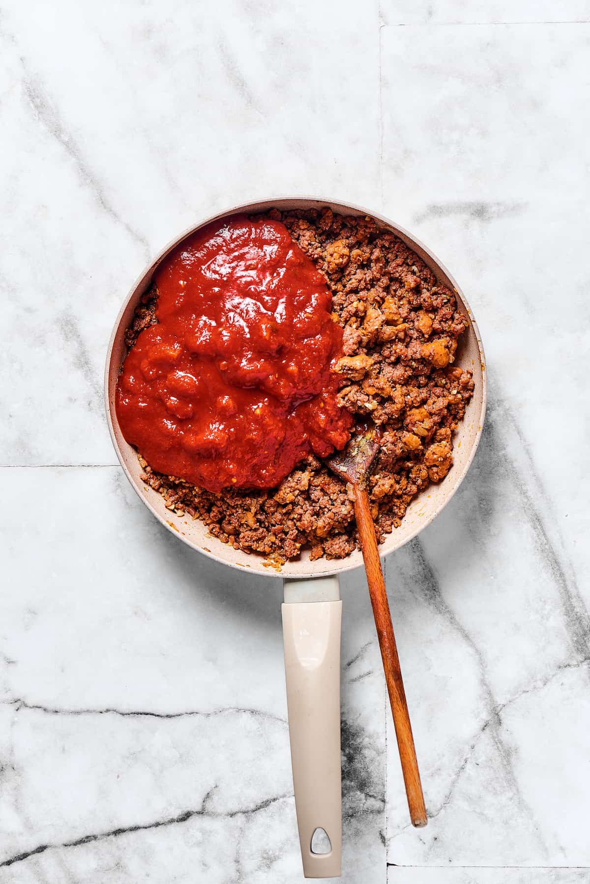Crushed tomatoes added to meat sauce in a skillet.