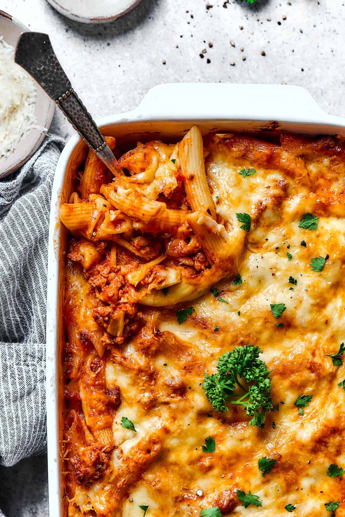 Scooping out a spoonful of baked mostaccioli from a large baking dish.