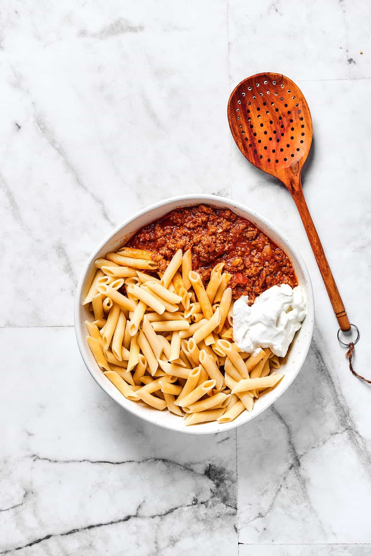 Mostaccioli pasta, ricotta, and meat sauce in a mixing bowl.