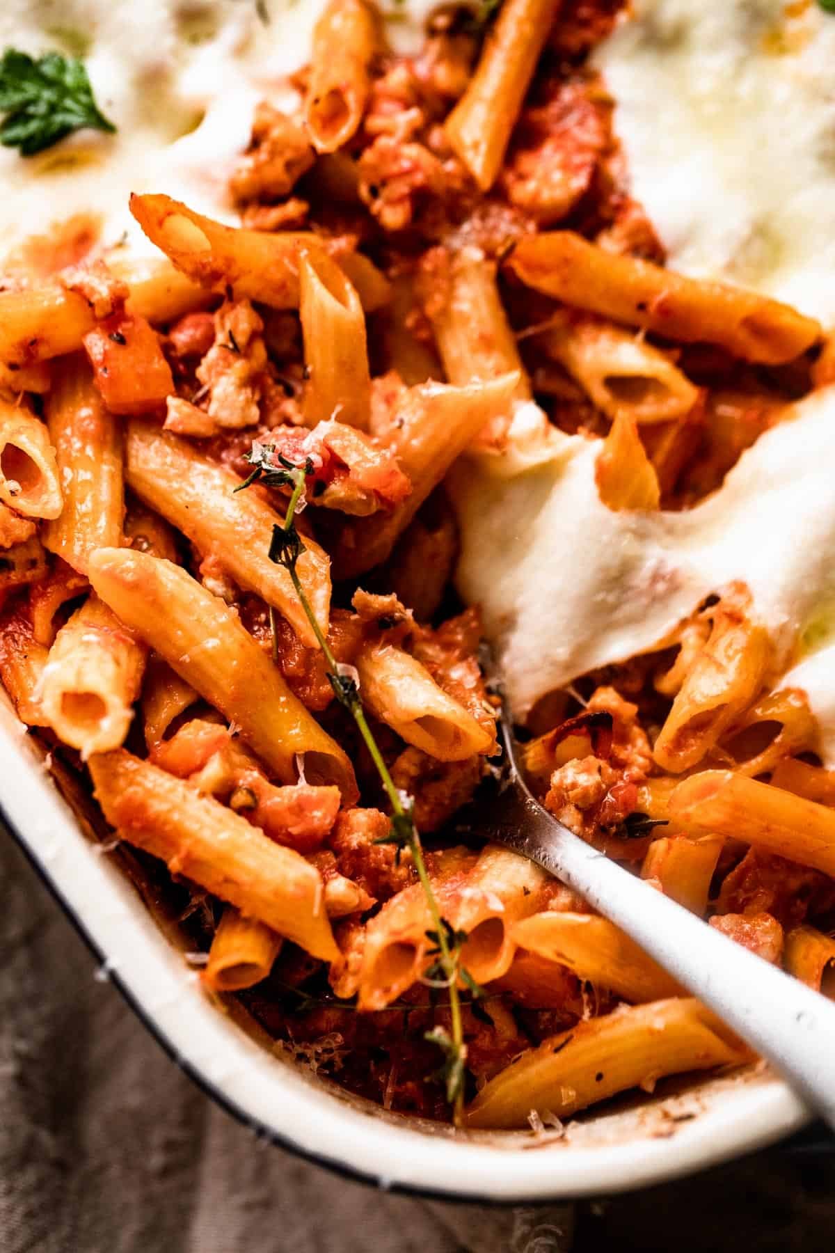 spooning out baked penne pasta from baking dish.