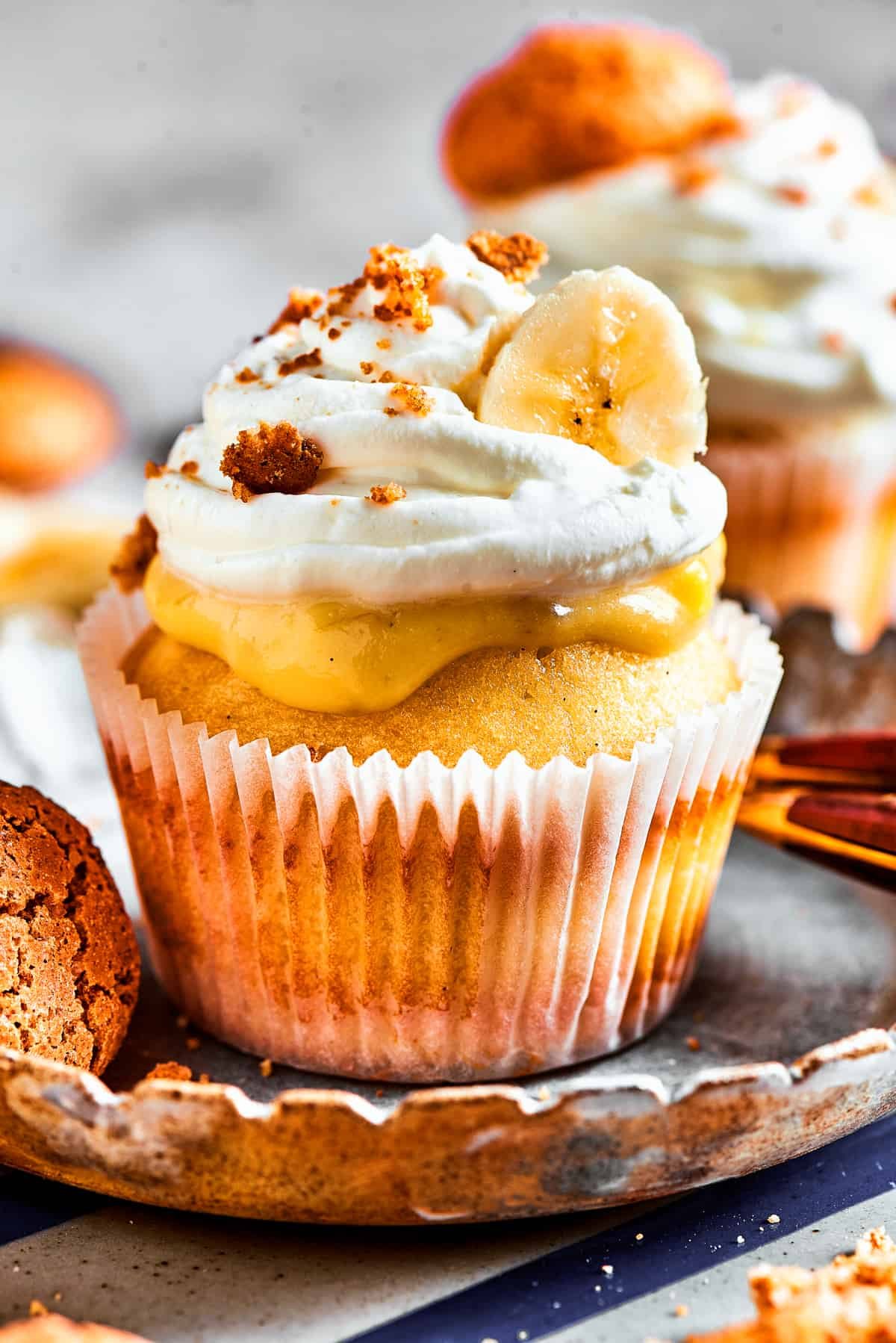 One banana pudding cupcake on a dessert plate. More cupcakes are in the background of the shot.