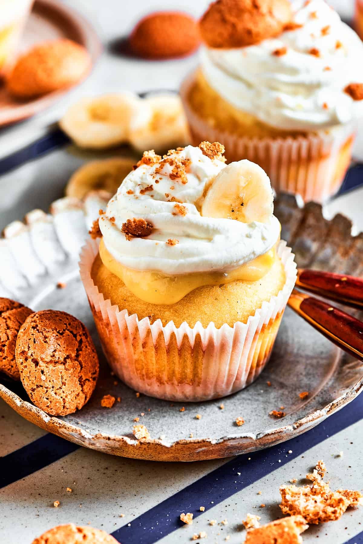 One banana pudding cupcake on a dessert plate. More cupcakes are in the background of the shot.