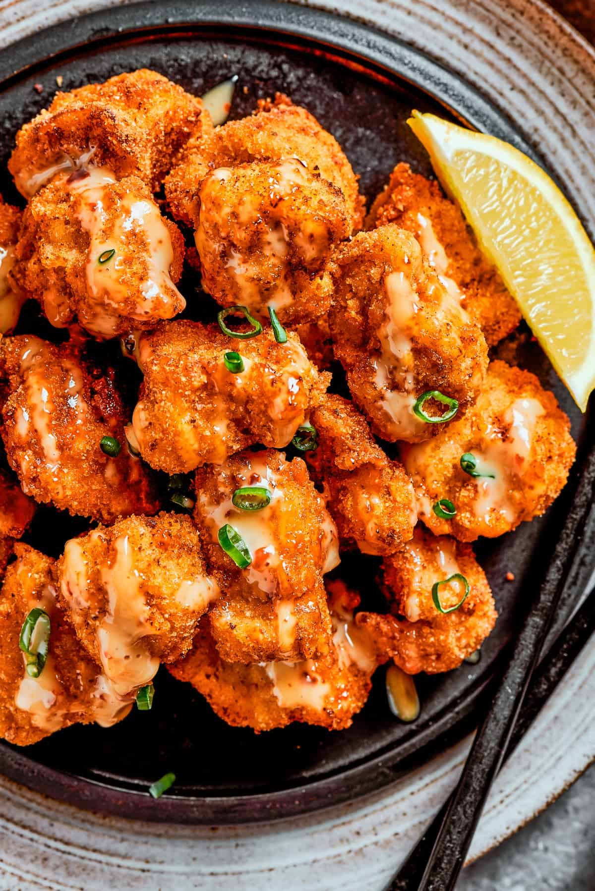 Overhead, close-up image of fried, crispy chicken bites topped with sauce and served with a lemon slice.