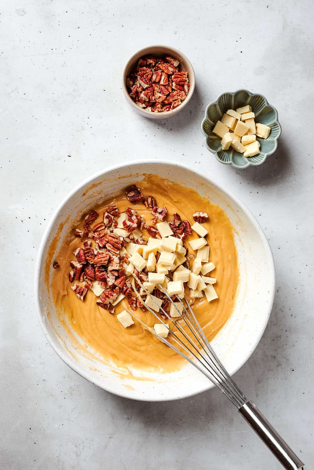 White chocolate chips and chopped pecans are stirred into a bowl of blondies batter.