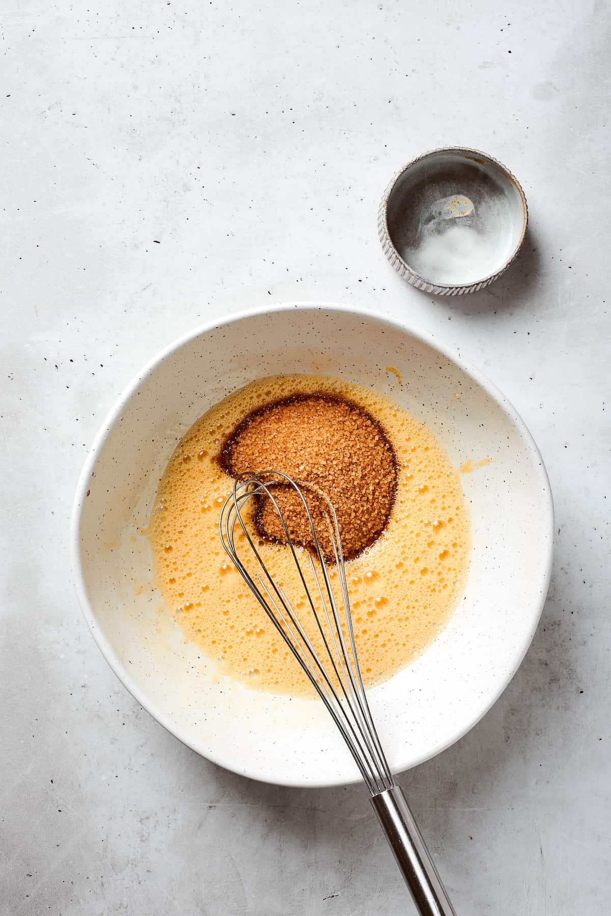Brown sugar is added to whisked eggs.