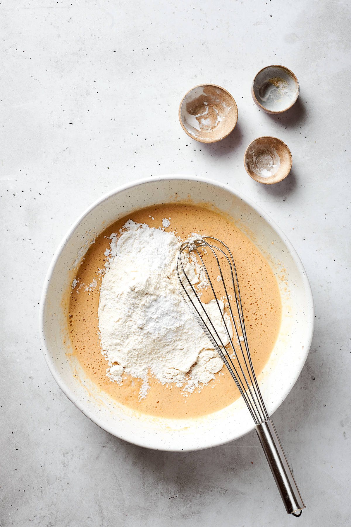 The dry mix is added to the top of a bowl of blonde brownies batter.