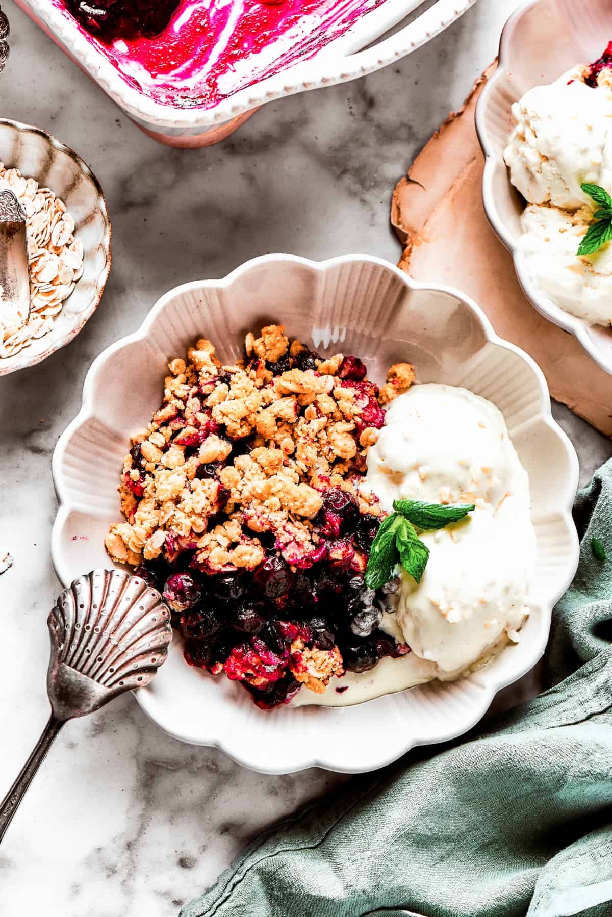 Blueberry crisp served in a bowl with two scoops of vanilla ice cream and a garnish of mint.