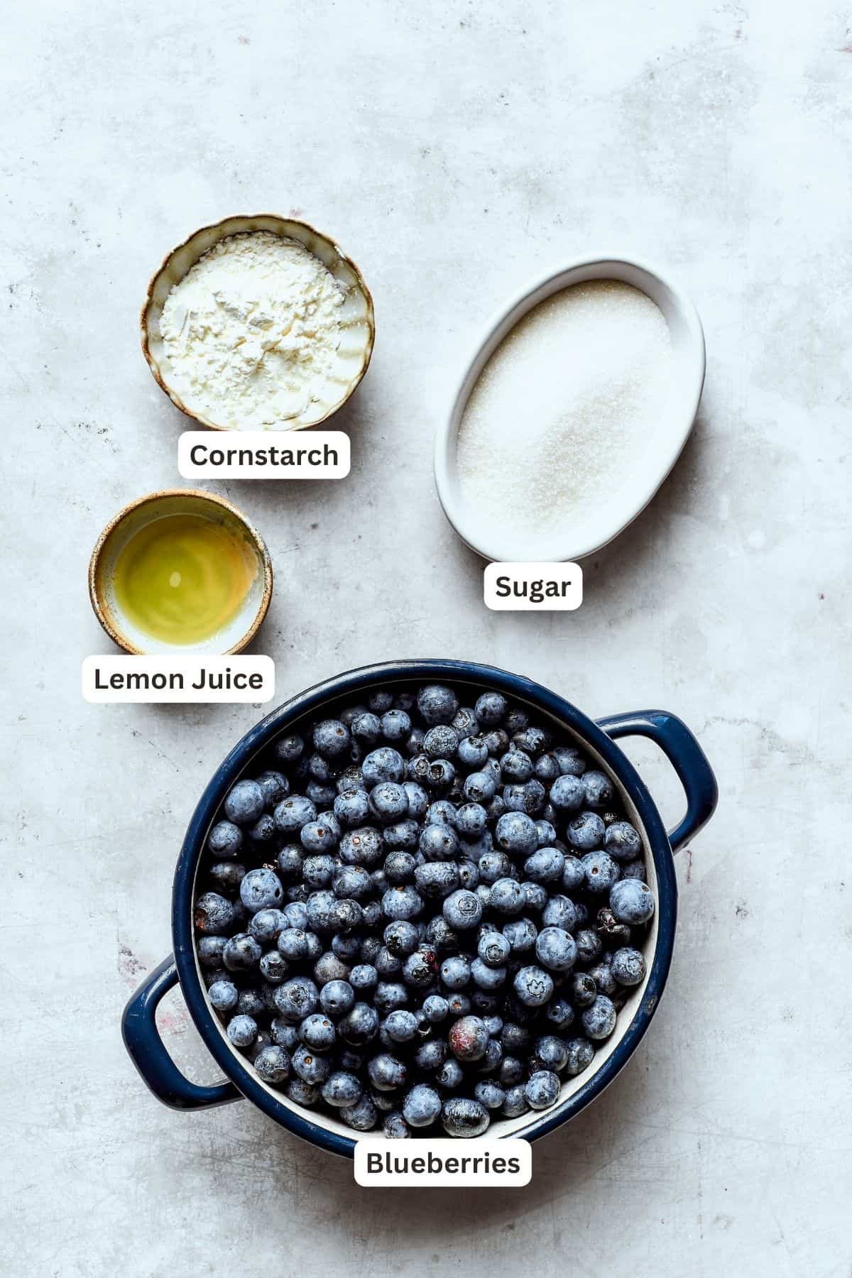 Ingredients for blueberry crisp filling are labeled and portioned: cornstarch, sugar, blueberries, lemon juice.