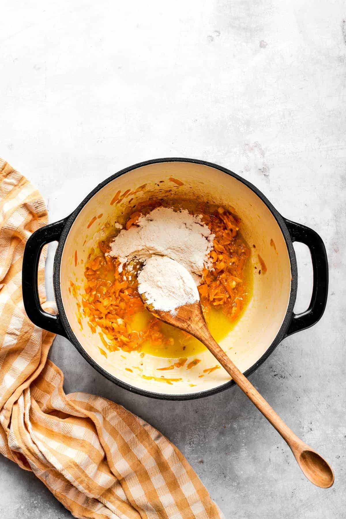 Adding flour to a pot with carrots and butter.