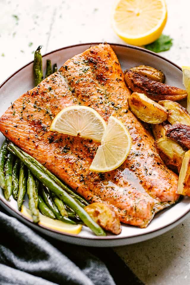 Broiled salmon plated with potatoes and greenbeans and garnished with lemon wedges