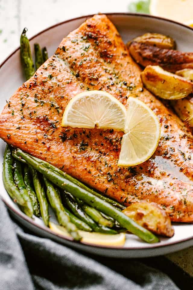 Broiled salmon plated with potatoes and greenbeans and garnished with lemon wedges