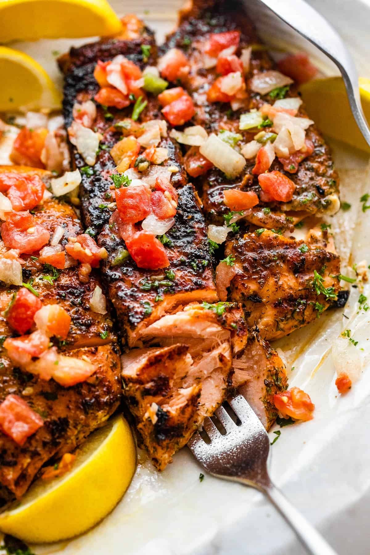 three grilled salmon fillets topped with tomatoes and onions