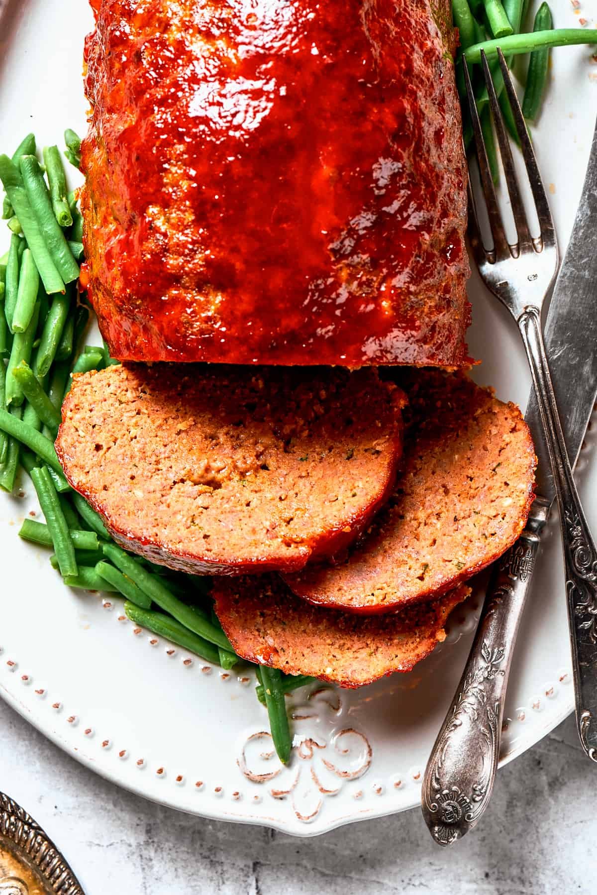 Overhead close-up photo of sliced brown sugar meatloaf served with green beans.