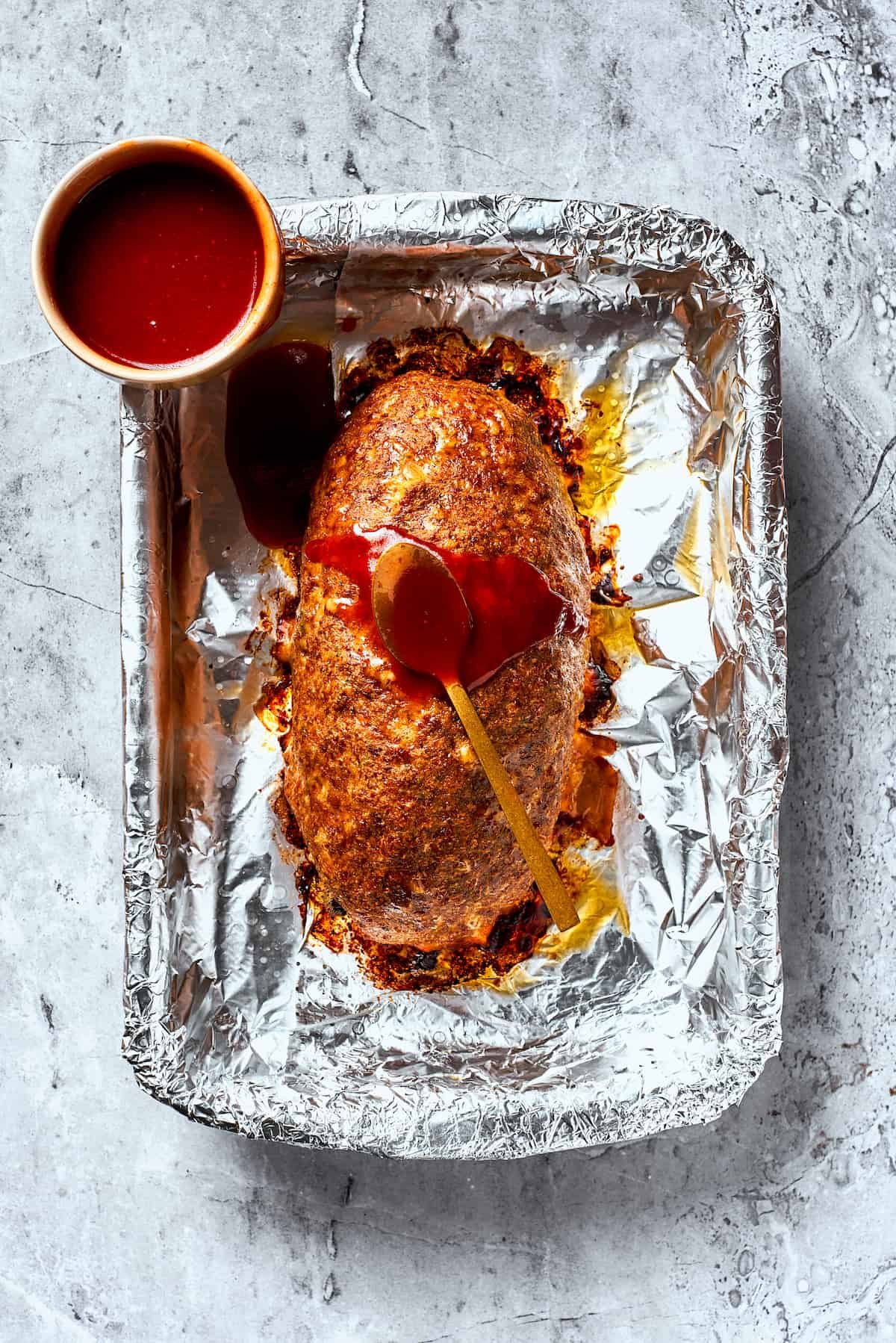 A brown sugar glaze is added to meatloaf on a foil lined pan.