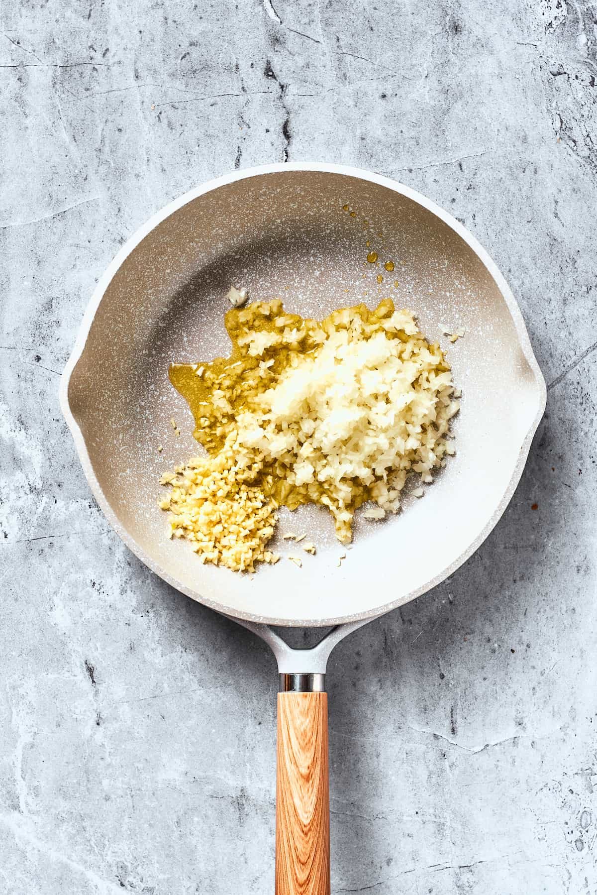 Onions and garlic cook in olive oil in a white pan.