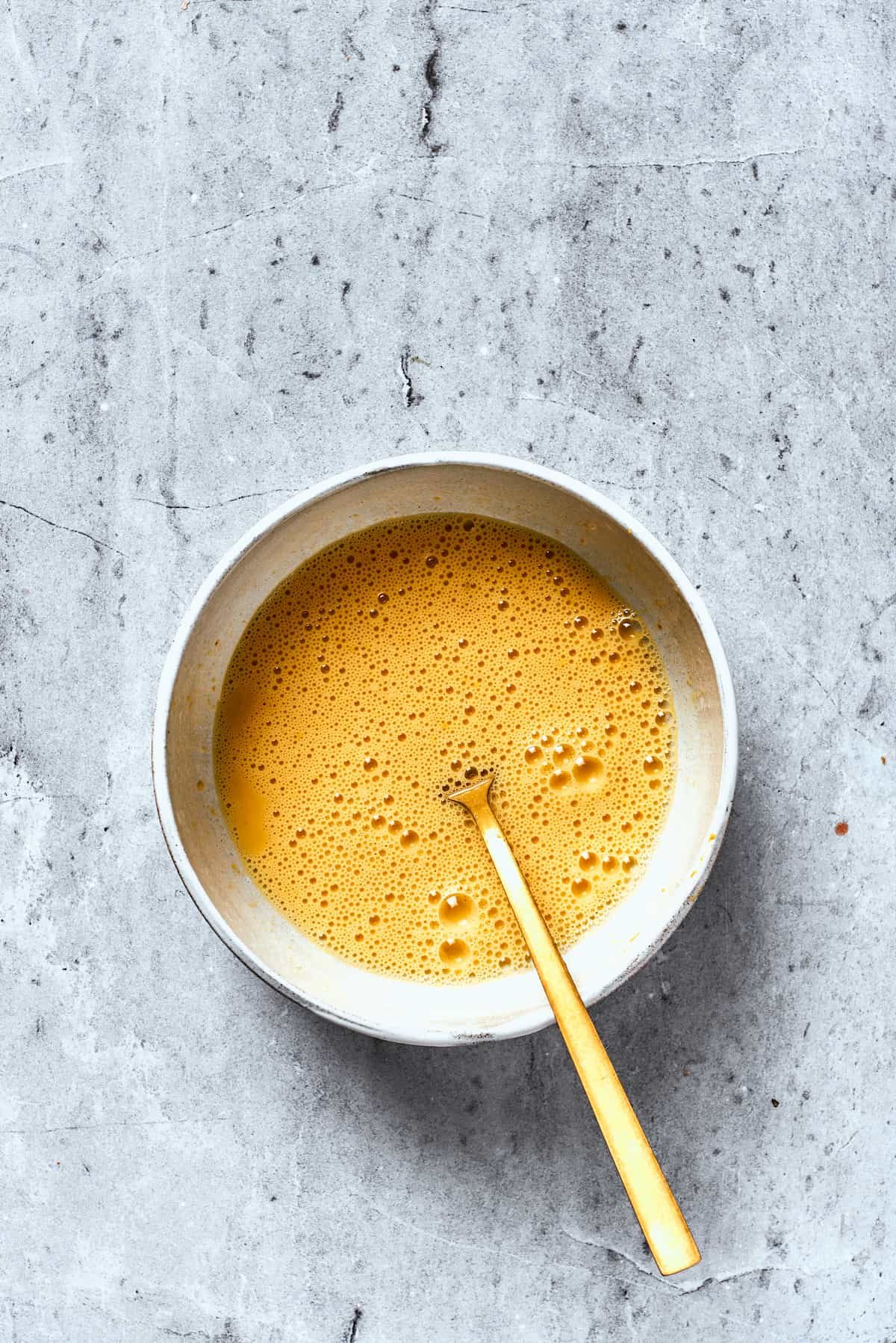 A white bowl holds whisked eggs.
