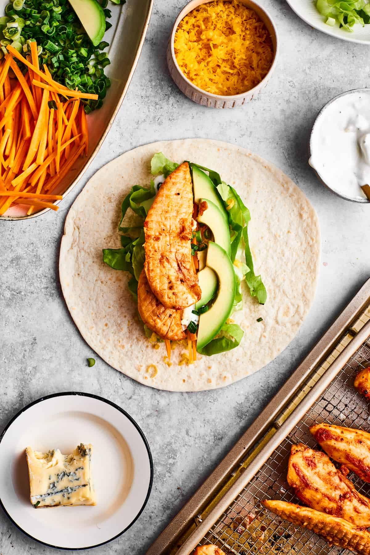 A seasoned chicken tender is placed on vegetables and a tortilla.